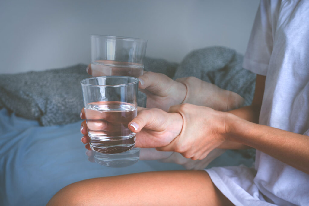 Person tries to hold glass of water but has alcohol shakes