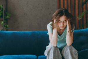 Woman sits on couch and nurses headache as she struggles with Prozac and weed use